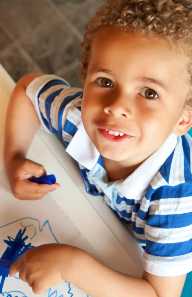 Criança olhando para cima e sorrindo, enquanto pinta desenho